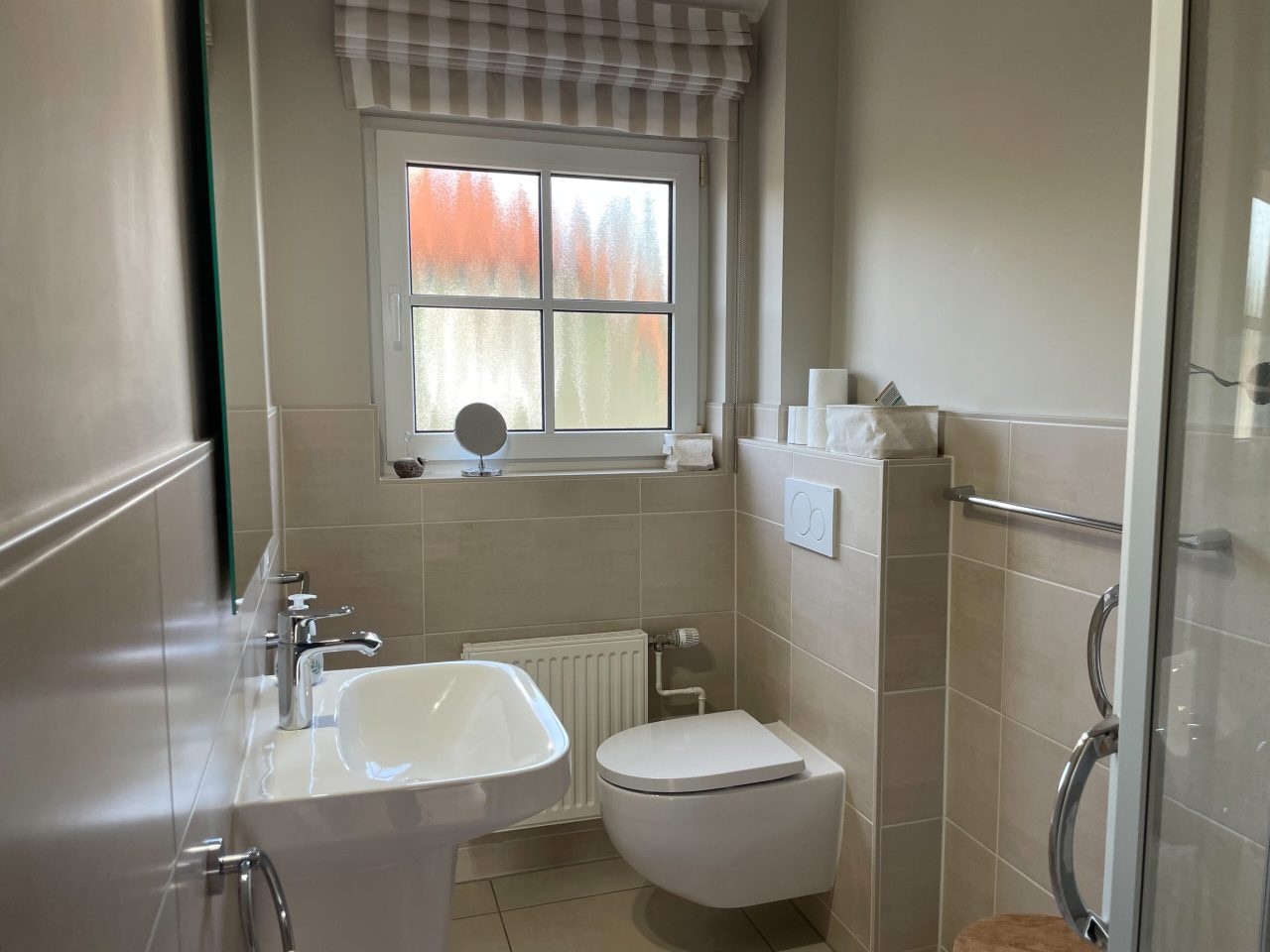 Badezimmer mit Glasdusche, Waschtisch, WC, Kosmetikspiegel und Fön